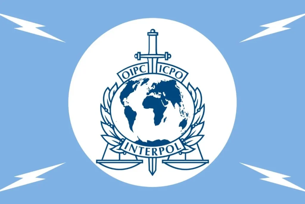 Flag of INTERPOL By INTERPOL - https://www.interpol.int/Who-we-are/Legal-framework/Name-and-logo, Fair use, https://en.wikipedia.org/w/index.php?curid=66958207